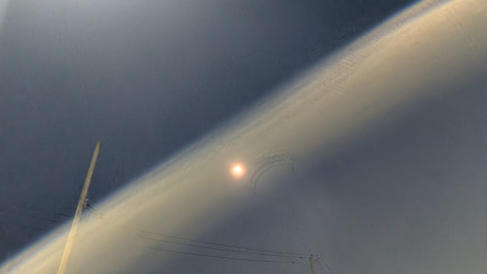 雲の切れ間から光が差し込み、小さく赤く滲んだ太陽が見える空の写真